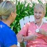 Older lady wearing a white LiveLife Pendant, smiling at carer.